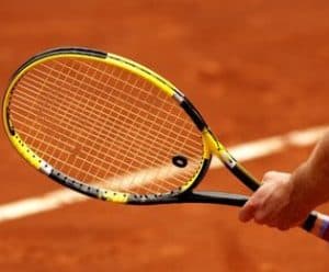 main tenant une raquette de tennis sur terre battue
