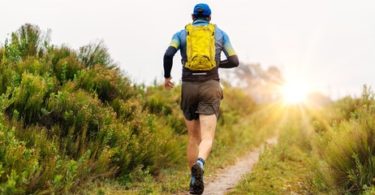 homme muni d'un sac à dos faisant un trail au coucher du soleil