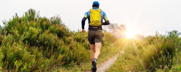 homme muni d'un sac à dos faisant un trail au coucher du soleil