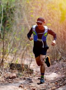 Jeune homme de face courant un trail dans la forêt